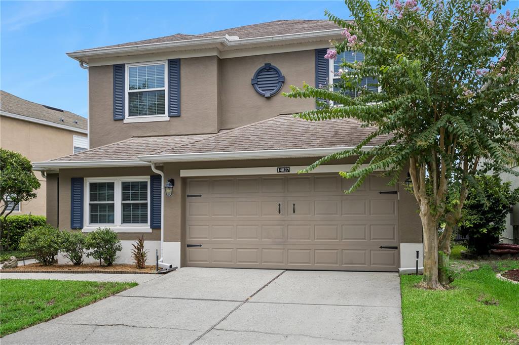 A two-story house with a tan stucco exterior, blue shutters, and a two-car garage — 14827 MASTHEAD LANDING CIRCLE, WINTER GARDEN, FL
