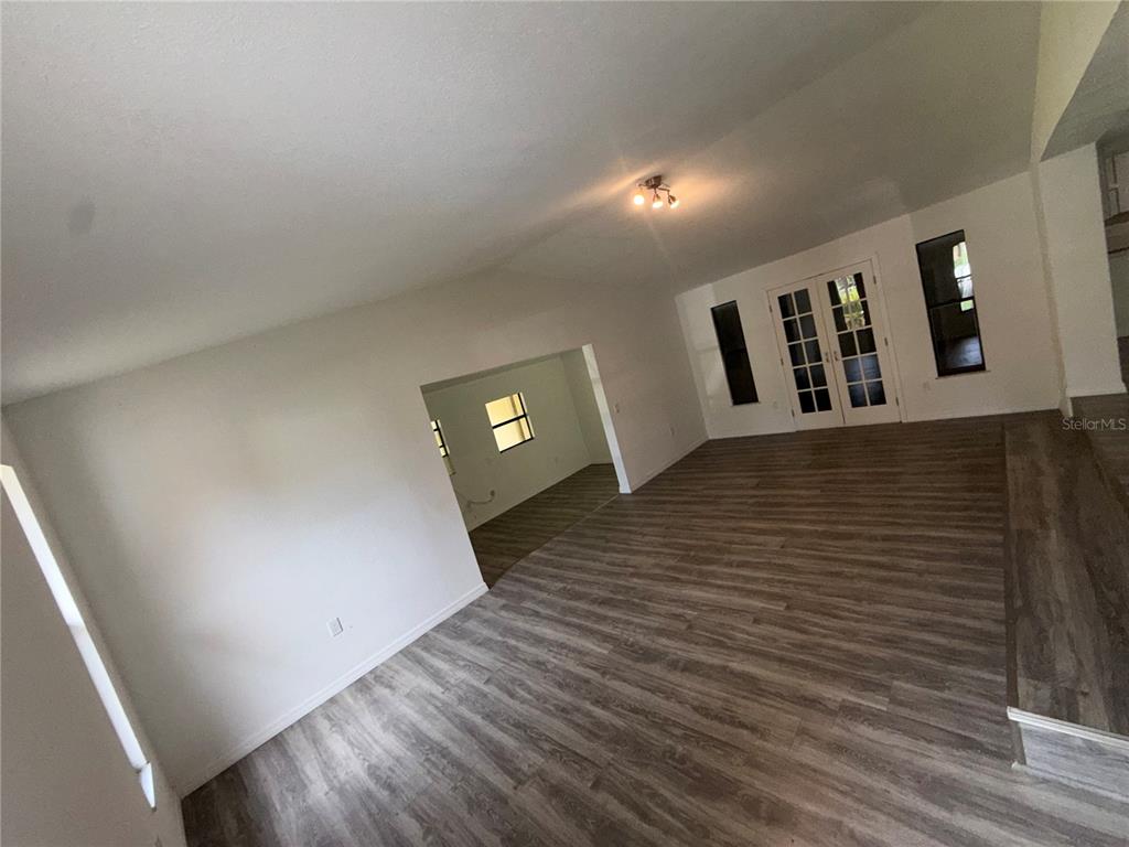 An open living area with wood-look flooring, white walls, and French doors leading outside — 17440 SE 37TH LANE, OCKLAWAHA, FL