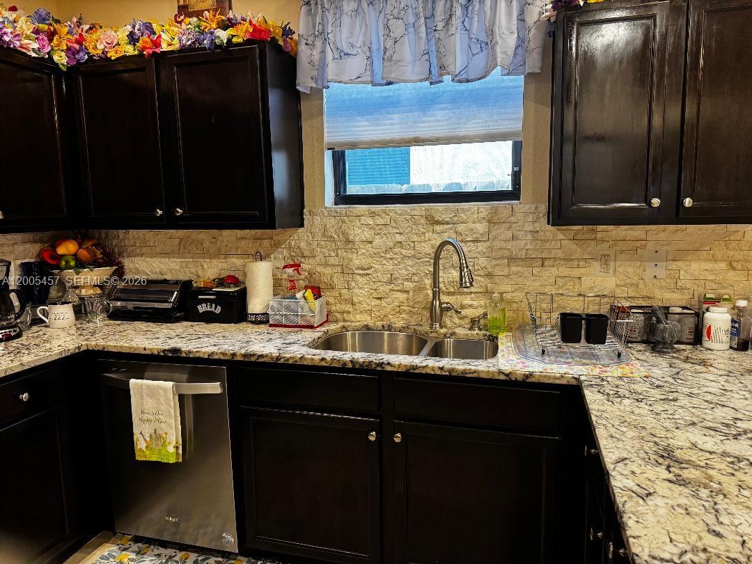 A kitchen features dark wood cabinets, granite countertops, a stone backsplash, and a double sink — 595 SE 33rd Ter, Homestead FL 33033, HOMESTEAD, FL
