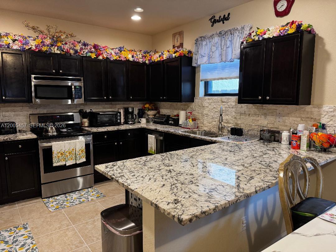 A kitchen features dark cabinets, granite countertops, stainless steel appliances, and a stone backsplash — 595 SE 33rd Ter, Homestead FL 33033, HOMESTEAD, FL