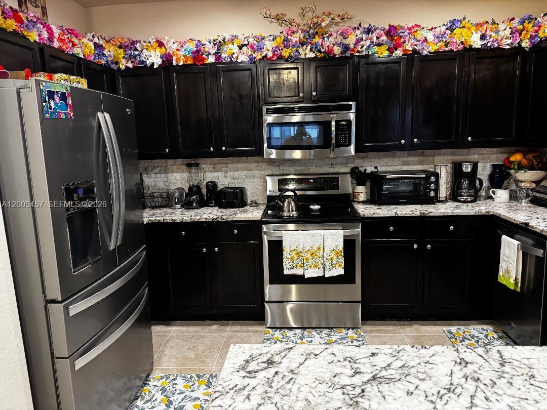 A kitchen features dark cabinets, stainless steel appliances, and a floral garland above the cupboards — 595 SE 33rd Ter, Homestead FL 33033, HOMESTEAD, FL
