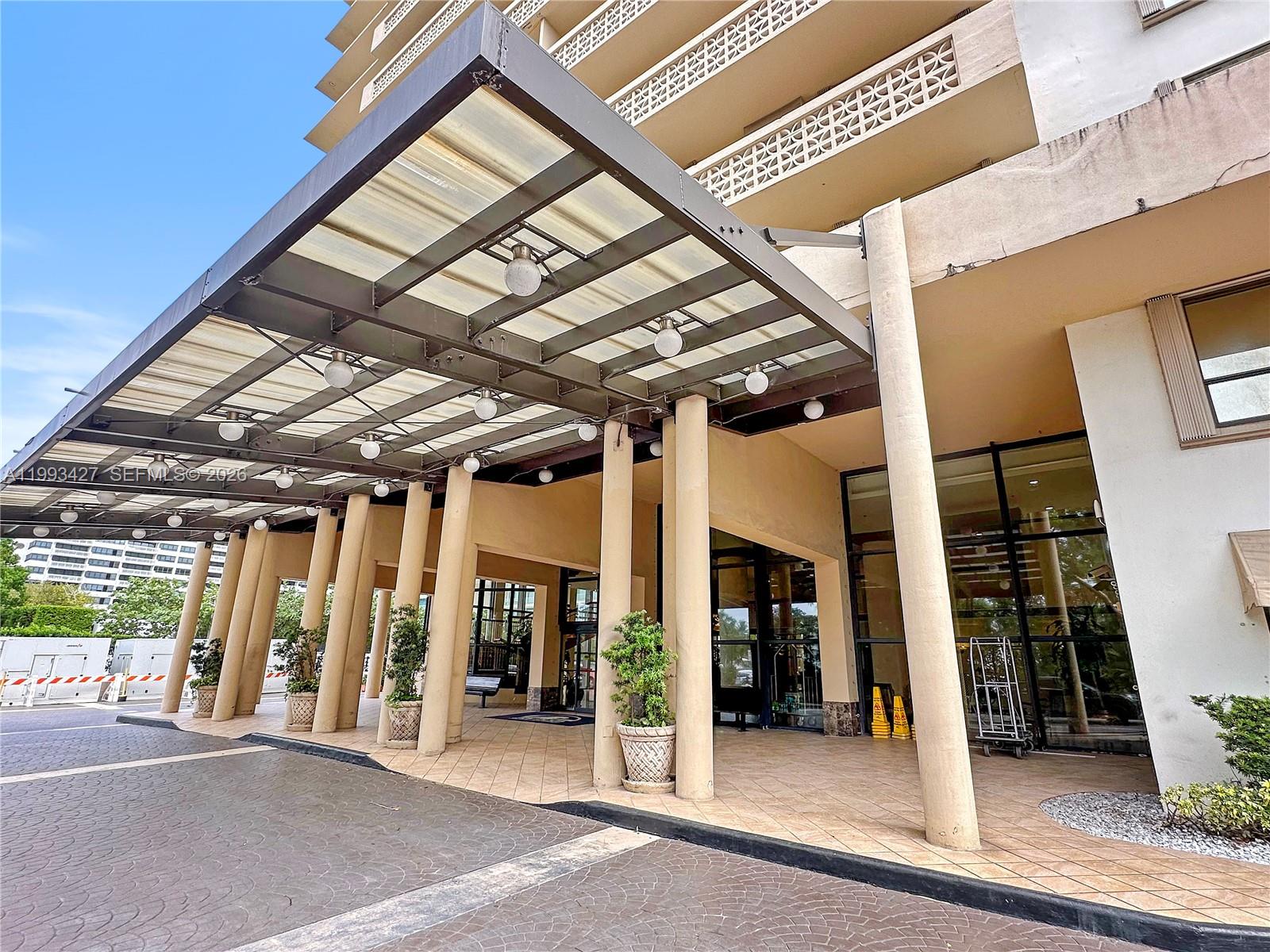 A covered porte-cochère entrance features a metal frame, glass panels, and multiple cylindrical columns — 10185 Collins Ave # 502, Bal Harbour FL 33154, BAL HARBOUR, FL