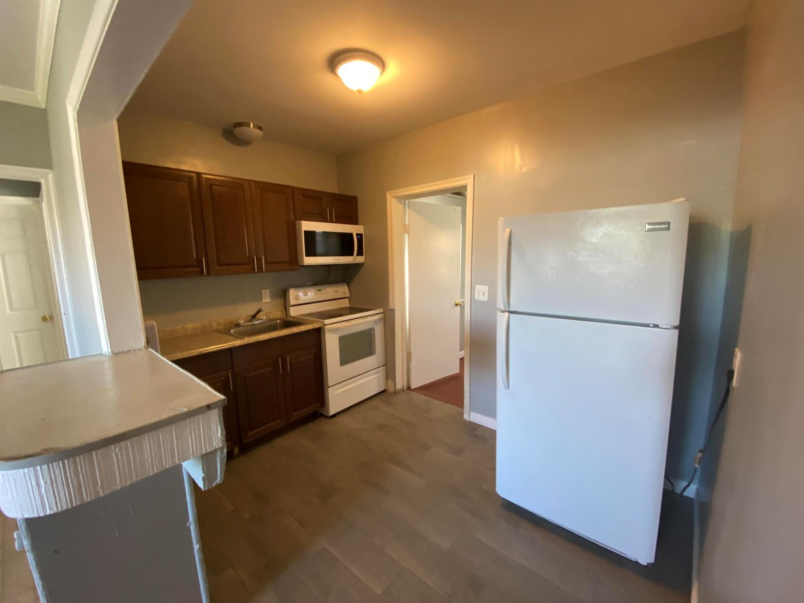 A kitchen features dark wood cabinets, white appliances, and light wood-look flooring — 119 W 25th Street # B, Riviera Beach FL 33404, RIVIERA BEACH, FL