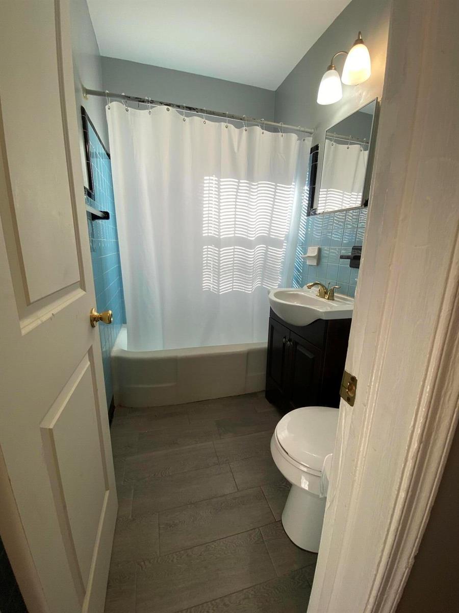 A small bathroom features a blue tiled shower, a dark vanity, and wood-look floor tiles — 119 W 25th Street # B, Riviera Beach FL 33404, RIVIERA BEACH, FL