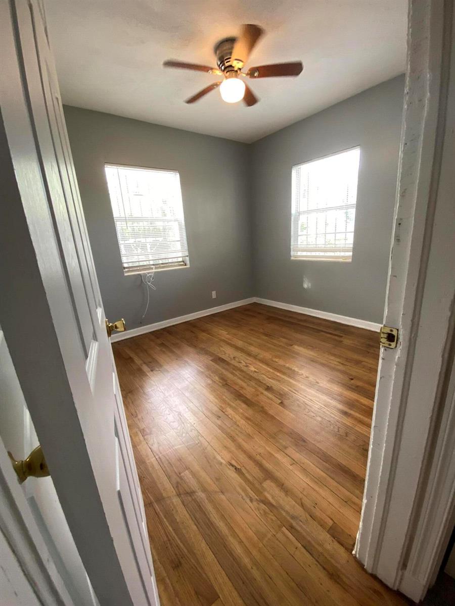 An empty bedroom with gray walls, hardwood flooring, two windows, and a ceiling fan — 119 W 25th Street # B, Riviera Beach FL 33404, RIVIERA BEACH, FL