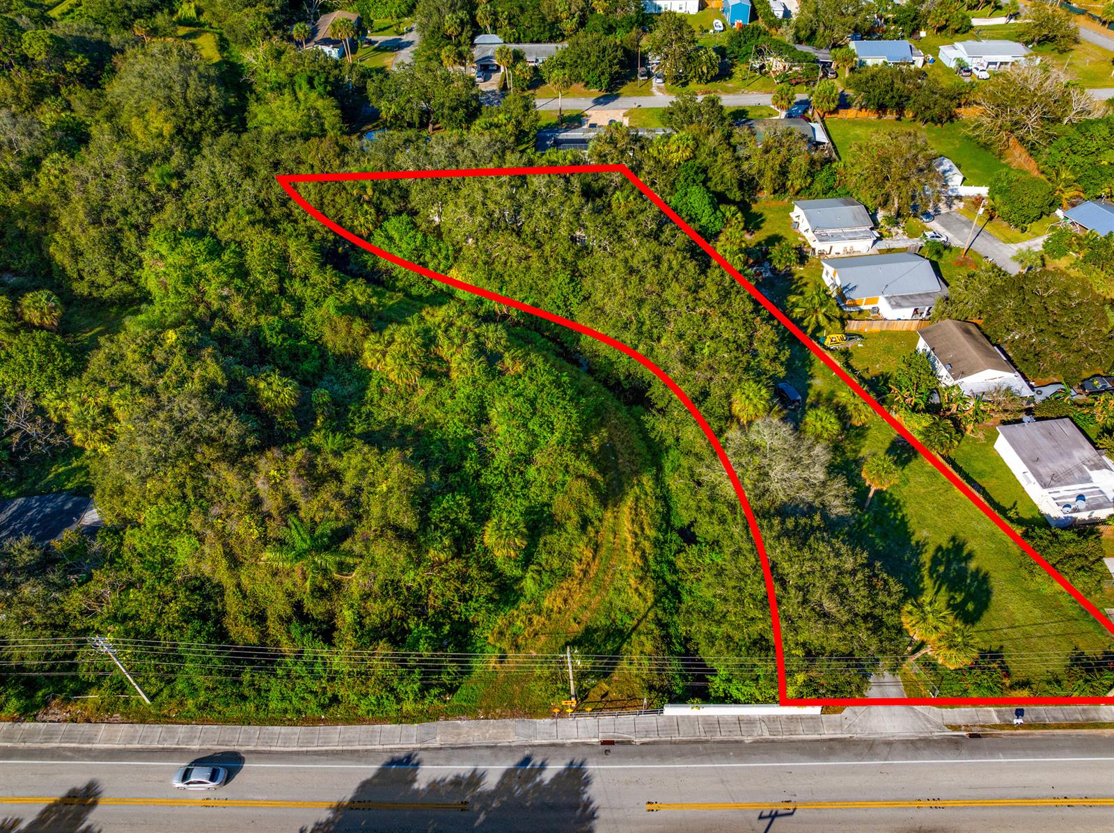 An aerial view shows a vacant, tree-covered lot outlined in red along a paved road — 2210 Saint Lucie Boulevard, Fort Pierce FL 34946, FORT PIERCE, FL