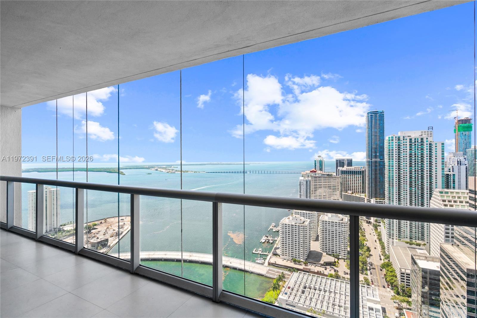 A high-rise balcony with a glass railing overlooks a city skyline and a large bay — 495 Brickell Ave # 4705, Miami FL 33131, MIAMI, FL