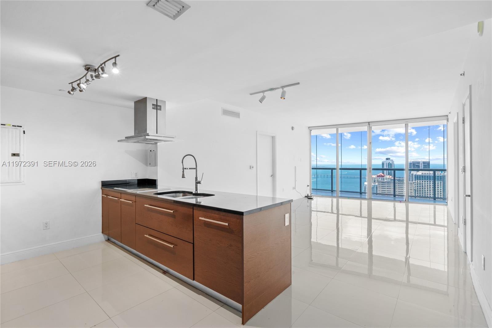 A modern kitchen with wood cabinets and a black countertop overlooks a balcony with water views — 495 Brickell Ave # 4705, Miami FL 33131, MIAMI, FL