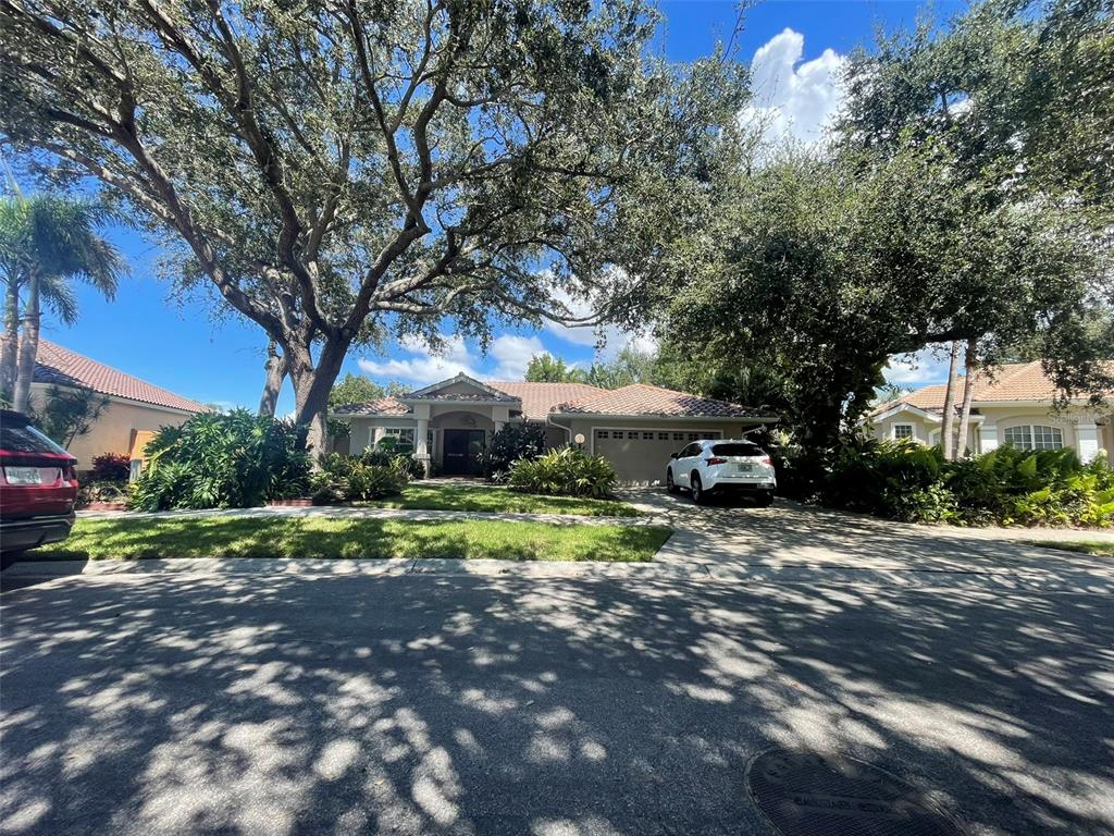 A single-story house with a tiled roof, a two-car garage, and large shade trees — 5607 OAK GROVE COURT, SARASOTA, FL