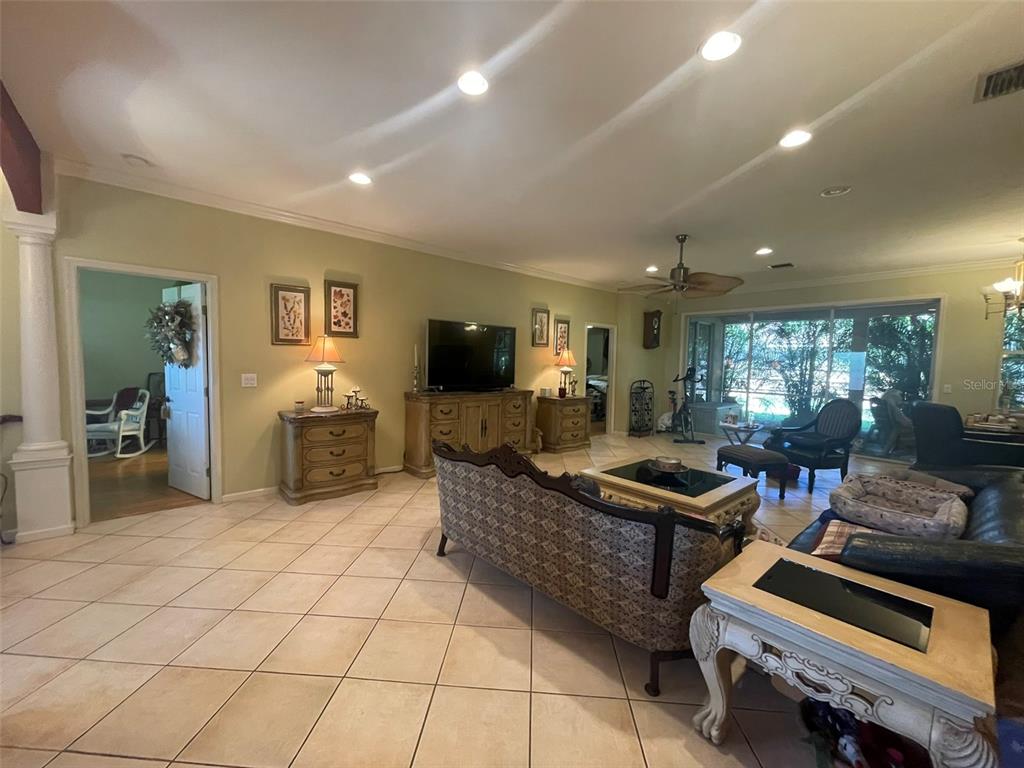 A spacious living room features tile flooring, a ceiling fan, and large windows overlooking greenery — 5607 OAK GROVE COURT, SARASOTA, FL