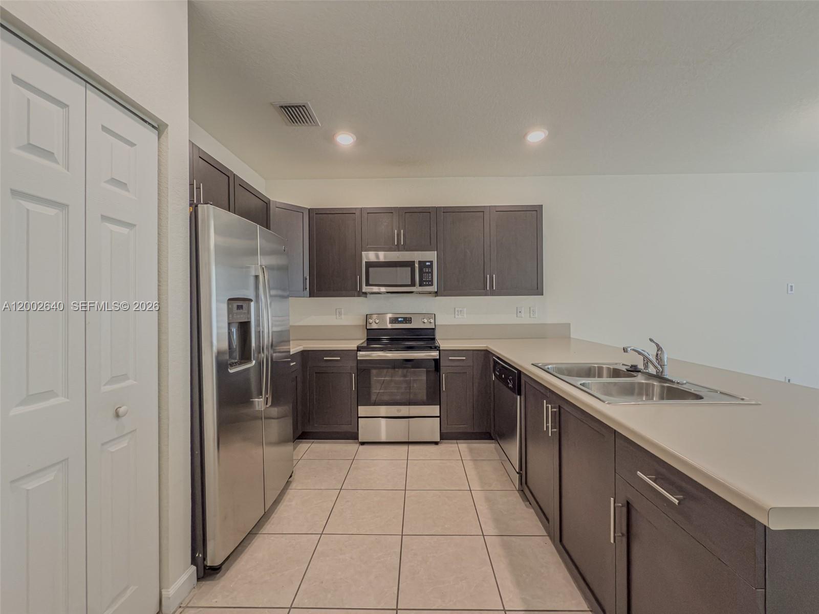 A kitchen features dark wood cabinets, stainless steel appliances, and light-colored tile flooring — 10629 W 32nd Ln, Miami Lakes FL 33018, MIAMI LAKES, FL