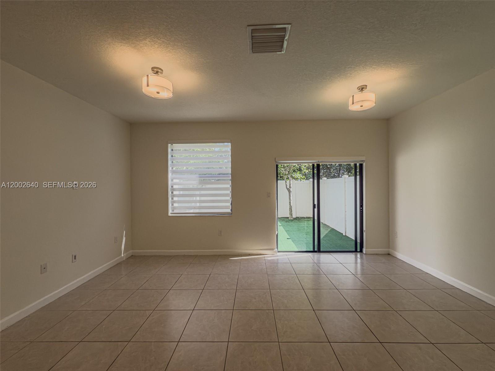 An empty room features beige tile flooring, two ceiling lights, a window, and sliding doors — 10629 W 32nd Ln, Miami Lakes FL 33018, MIAMI LAKES, FL