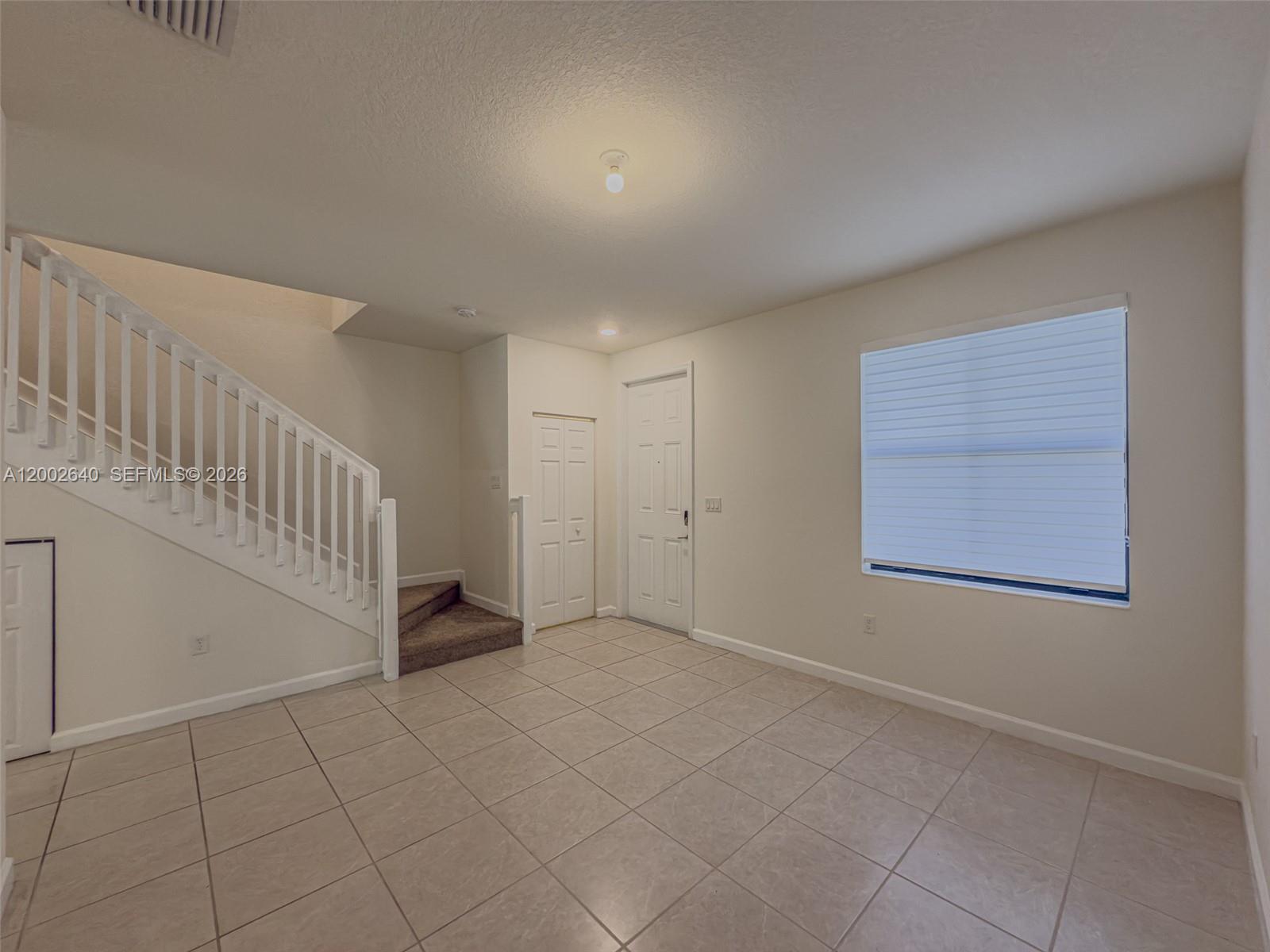 An empty room features beige tile flooring, a staircase with white railings, and a door — 10629 W 32nd Ln, Miami Lakes FL 33018, MIAMI LAKES, FL