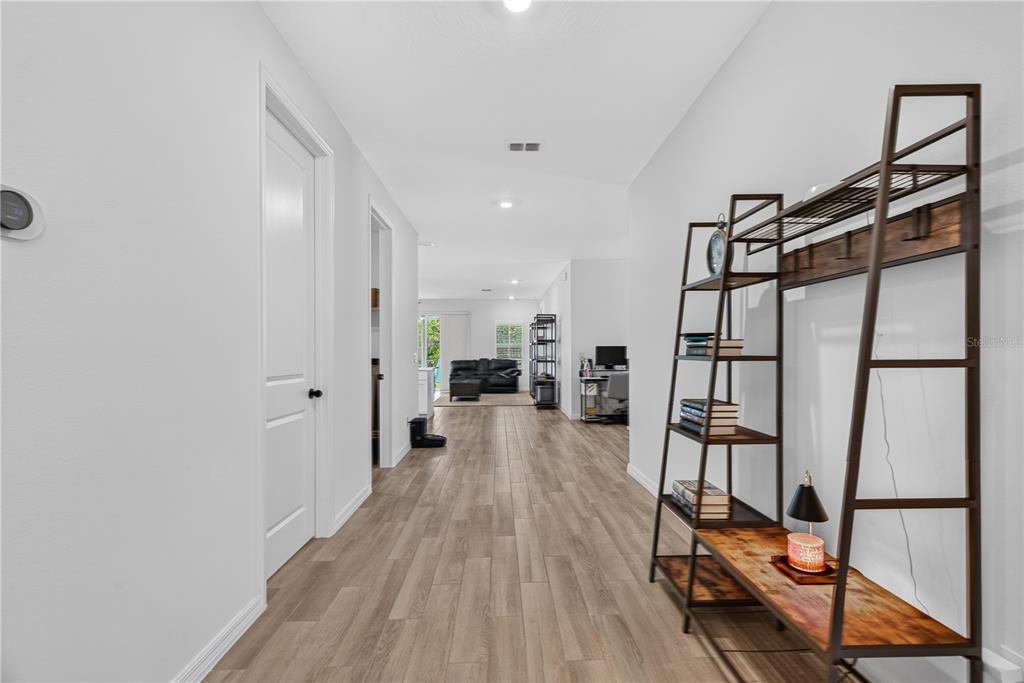 A hallway with wood-look flooring leads to an open living area with a dark sofa — 1113 PEARL TREE ROAD, DELTONA, FL