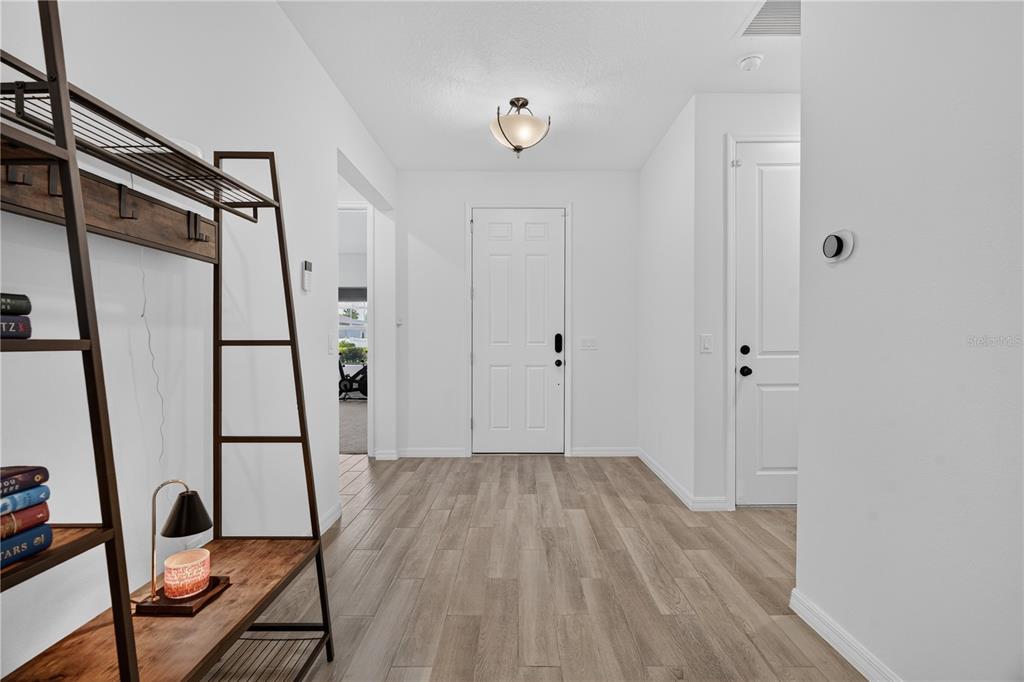An entryway features light wood-look flooring, a white front door, and a metal shelving unit — 1113 PEARL TREE ROAD, DELTONA, FL
