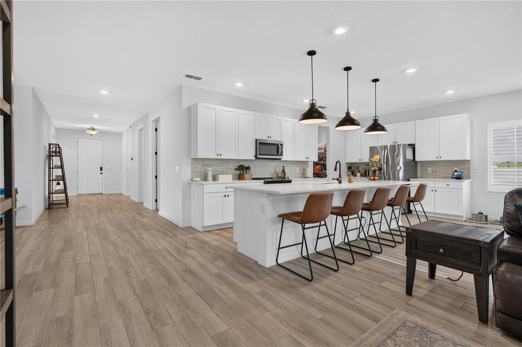 A modern kitchen features white cabinets, a large island with bar seating, and wood-look flooring — 1113 PEARL TREE ROAD, DELTONA, FL