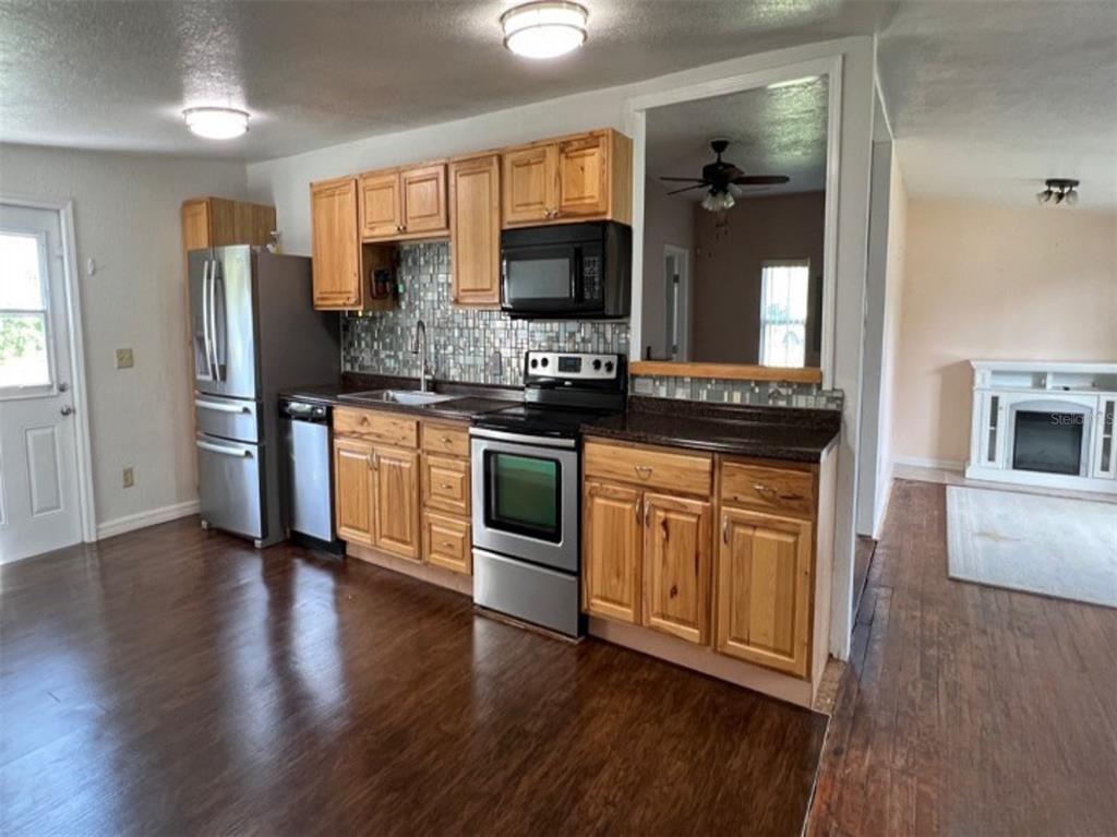 A kitchen features wood cabinets, stainless steel appliances, a mosaic backsplash, and dark wood flooring — 34 S DEAN ROAD, ORLANDO, FL