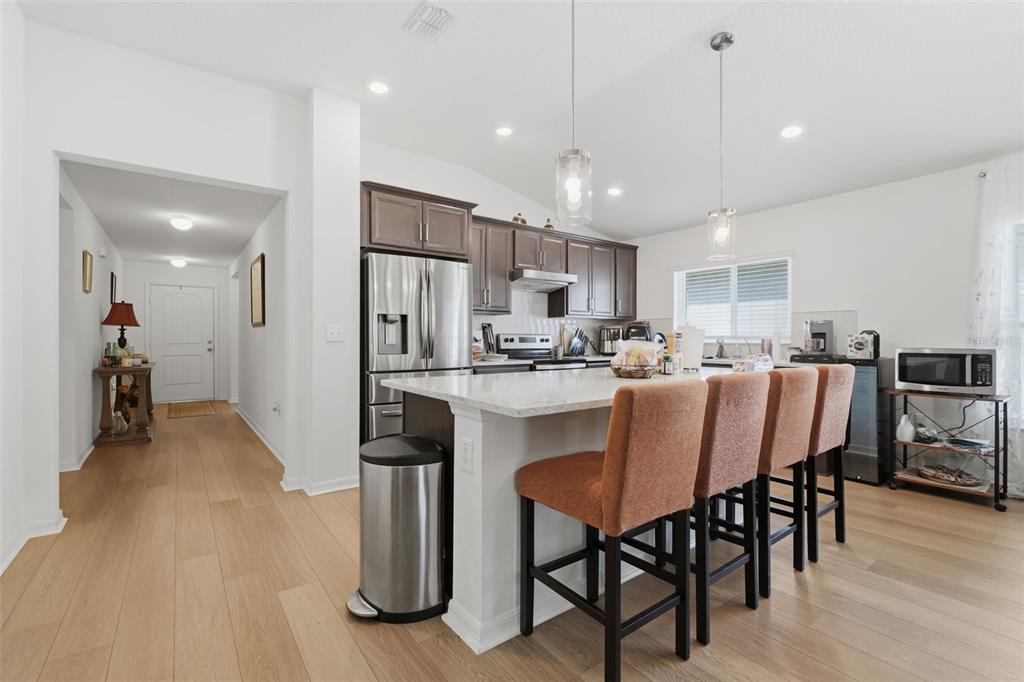 A modern kitchen features a white island with four stools, stainless steel appliances, and wood flooring — 13085 THATCH PALM WAY, ORLANDO, FL