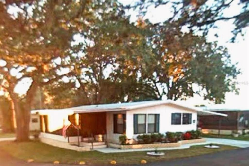 A single-story mobile home with white siding sits under large trees on a grassy lot — 900 AQUA ISLES BOULEVARD UNIT B21, LABELLE, FL