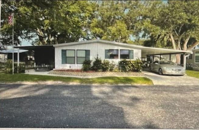 A single-story manufactured home with a carport, white siding, and green shutters under large trees — 900 AQUA ISLES BOULEVARD UNIT B21, LABELLE, FL