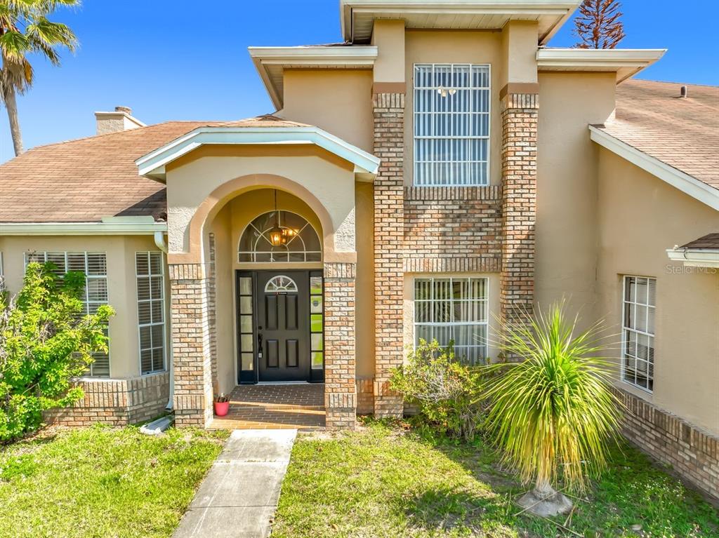 A tan two-story house features a brick-accented entryway with an arched doorway and walkway — 2645 ROLLING BROAK DRIVE, ORLANDO, FL