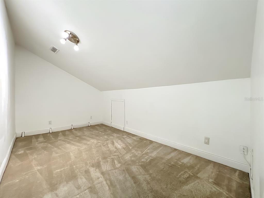 An empty room with beige carpet, white walls, a sloped ceiling, and a small access door — 2645 ROLLING BROAK DRIVE, ORLANDO, FL