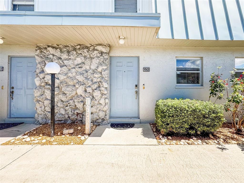 The exterior of a residential building features a stone facade, two doors, and landscaping — 6777 WINKLER ROAD UNIT 150, FORT MYERS, FL