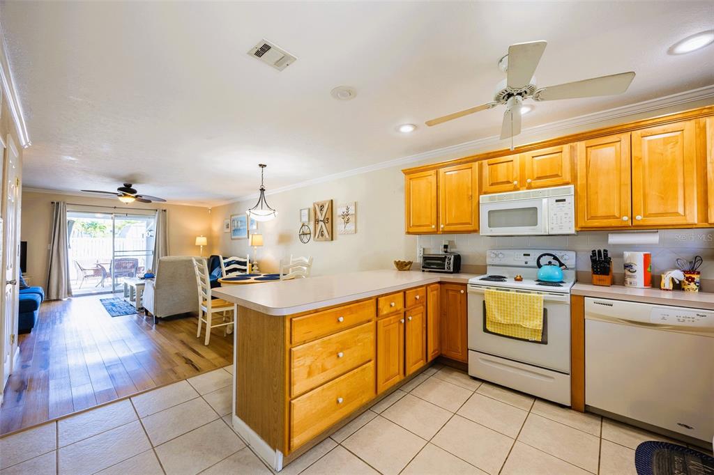 A kitchen with wood cabinets and white appliances opens into a living area with flooring — 6777 WINKLER ROAD UNIT 150, FORT MYERS, FL