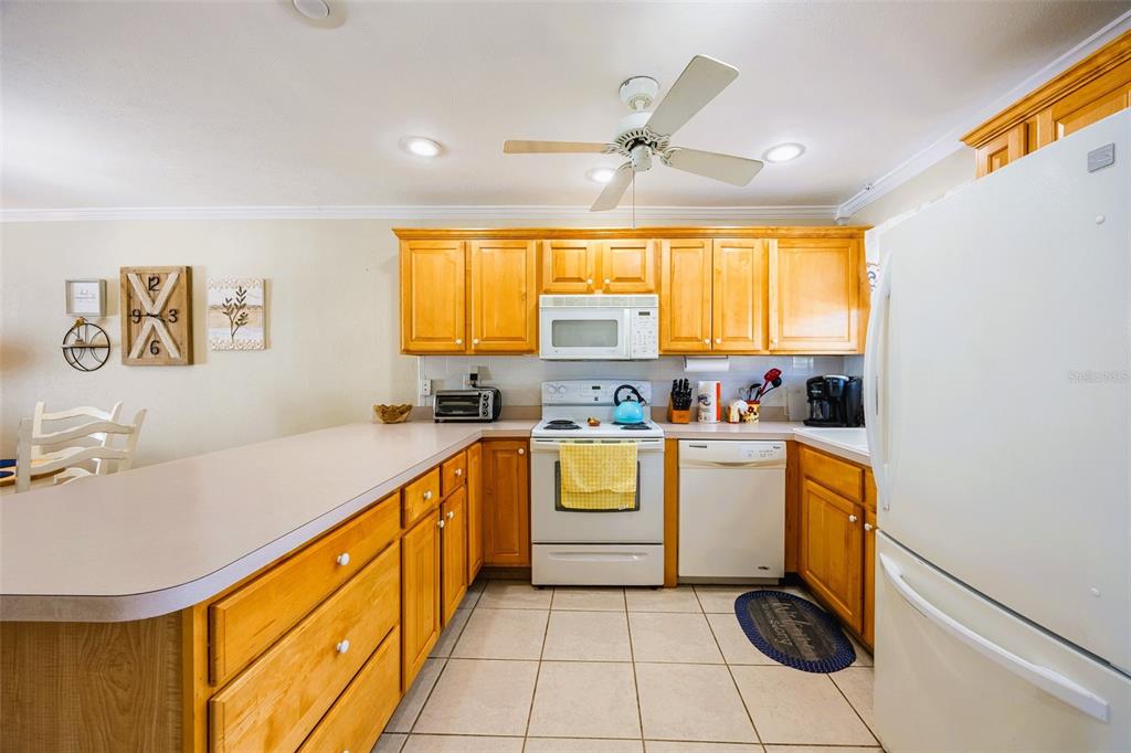 A kitchen features light wood cabinets, white appliances, a breakfast bar, and tiled flooring — 6777 WINKLER ROAD UNIT 150, FORT MYERS, FL