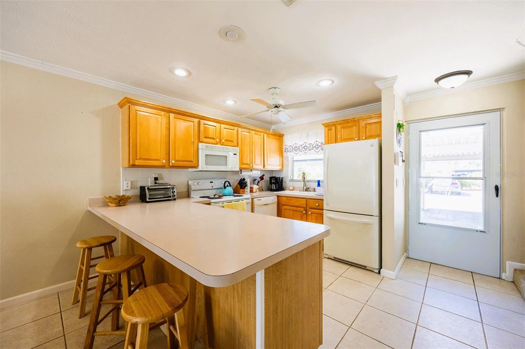 A kitchen with light-colored tile flooring, wood cabinets, a breakfast bar, and a white refrigerator — 6777 WINKLER ROAD UNIT 150, FORT MYERS, FL