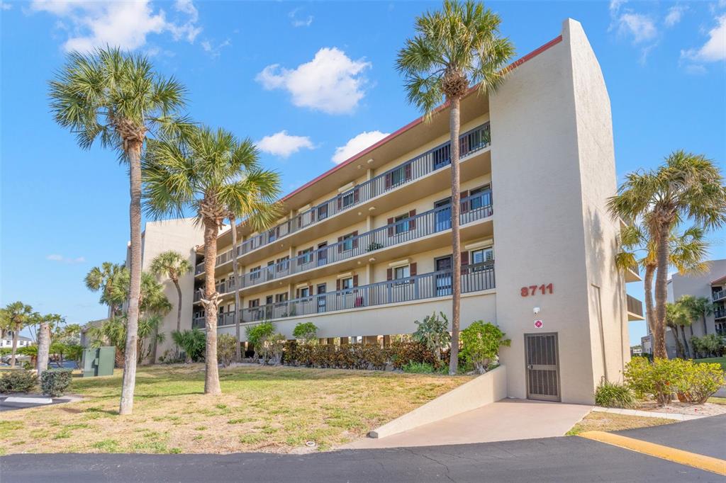 A multi-story apartment building with balconies and palm trees under a blue sky — 8711 BLIND PASS ROAD UNIT 104A, ST PETERSBURG, FL