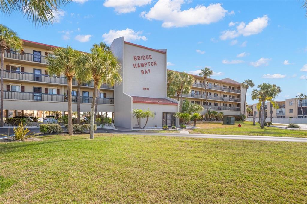 The exterior of a multi-story apartment building features a central entrance with palm trees — 8711 BLIND PASS ROAD UNIT 104A, ST PETERSBURG, FL
