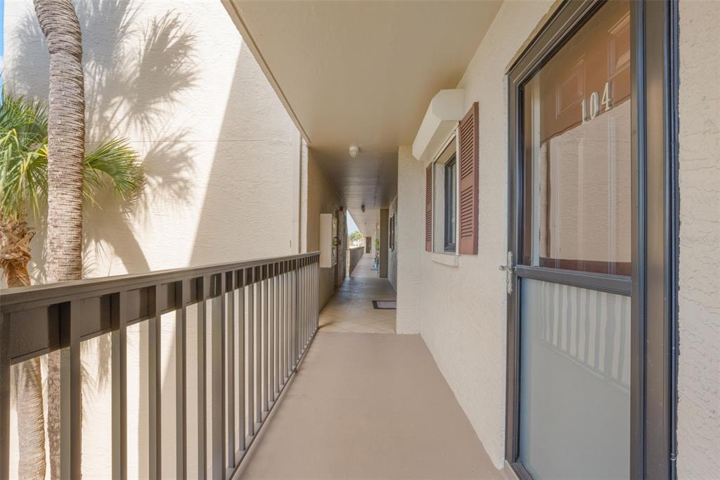 An exterior apartment hallway features a metal railing, a palm tree, and a door labeled 104 — 8711 BLIND PASS ROAD UNIT 104A, ST PETERSBURG, FL