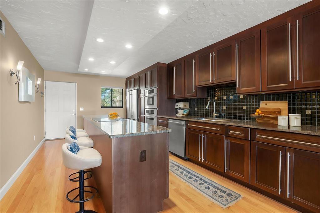 A kitchen with dark wood cabinets, a granite island, and bar seating on hardwood floors — 8711 BLIND PASS ROAD UNIT 104A, ST PETERSBURG, FL