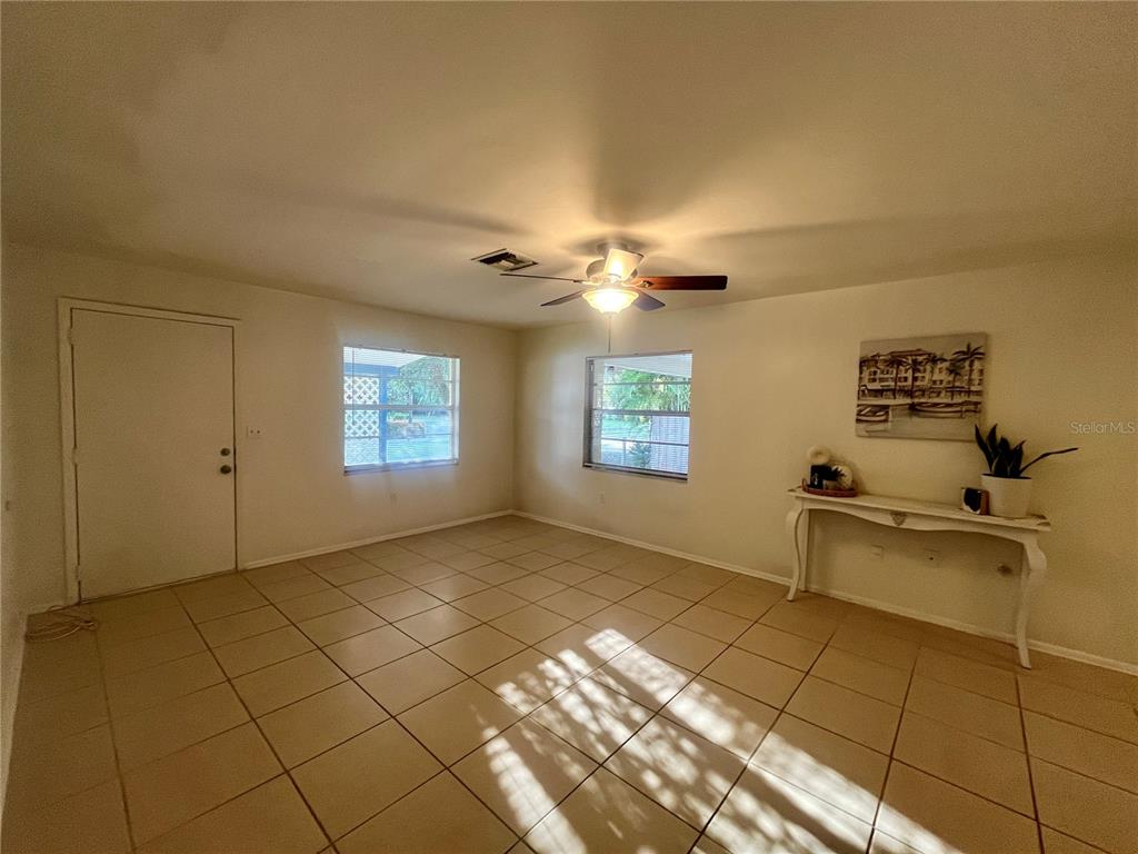 A living room with light-colored tile flooring, two windows, a ceiling fan, and a console table — 705 BAYOU AVENUE, TARPON SPRINGS, FL