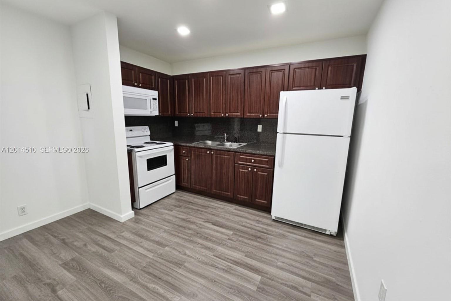 A kitchen features dark wood cabinets, white appliances, and gray wood-look flooring — 6961 W 14th Ct # 103, Hialeah FL 33014, HIALEAH, FL