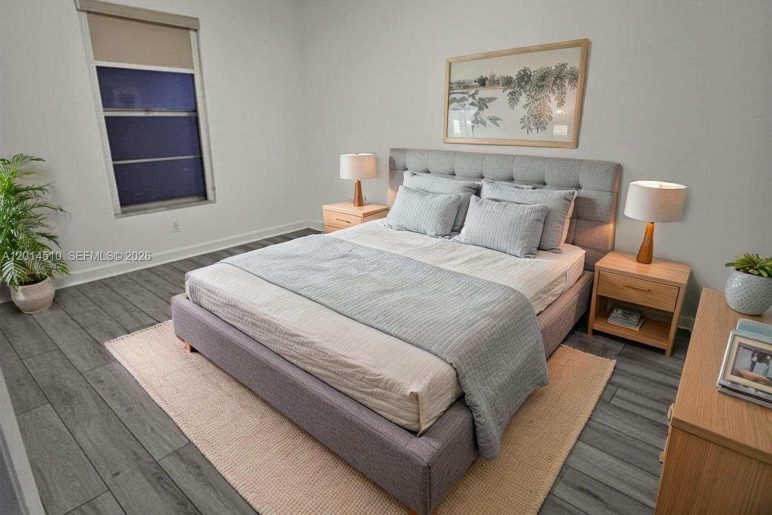 A bedroom features a gray upholstered bed, light wood nightstands, and gray wood-look flooring — 6961 W 14th Ct # 103, Hialeah FL 33014, HIALEAH, FL