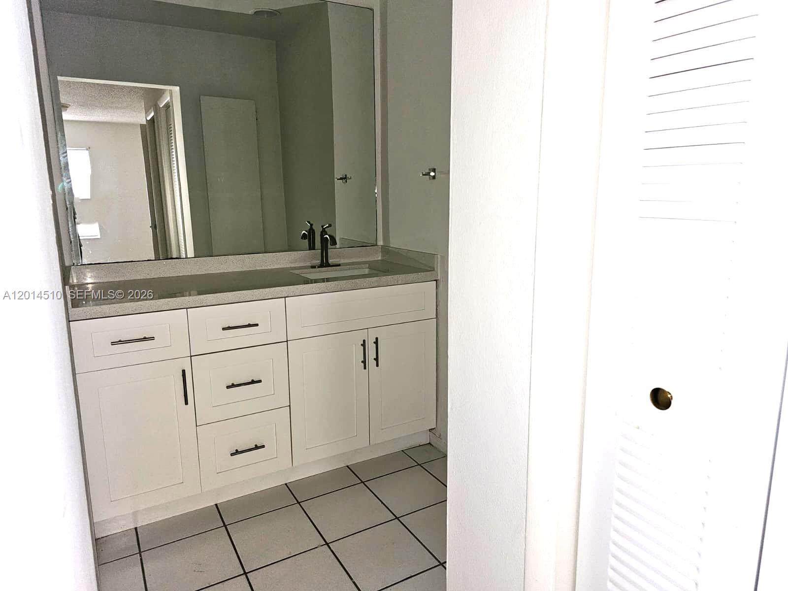 A bathroom features a white vanity with a stone countertop, a mirror, and tiled flooring — 6961 W 14th Ct # 103, Hialeah FL 33014, HIALEAH, FL