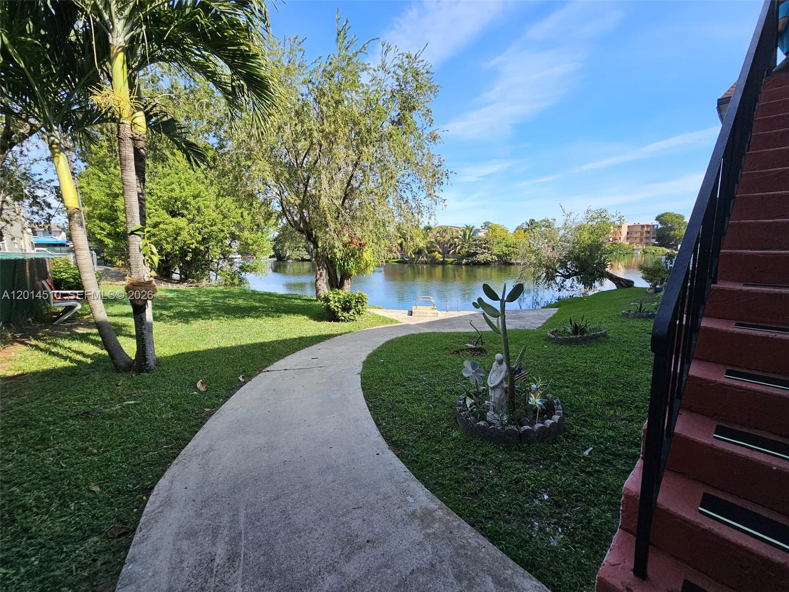 A concrete path leads through a grassy yard toward a lake with trees — 6961 W 14th Ct # 103, Hialeah FL 33014, HIALEAH, FL