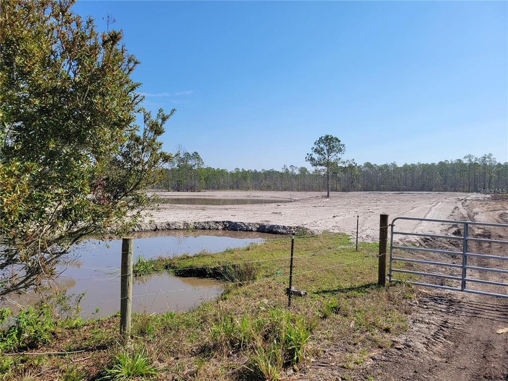 A fenced rural property features a small pond and a large, cleared sandy area — 1051 OMEGA RANCH ROAD UNIT 15, NEW SMYRNA BEACH, FL