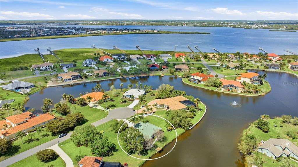 An aerial view shows a house with a green roof circled on a waterfront lot — 6115 9TH AVENUE CIRCLE NE, BRADENTON, FL