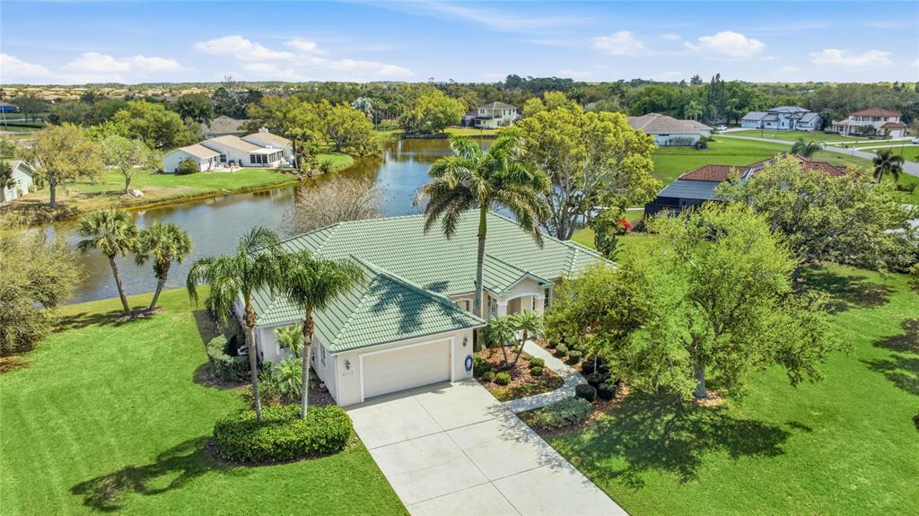 An aerial view of a single-story house with a green tile roof and a lake — 6115 9TH AVENUE CIRCLE NE, BRADENTON, FL