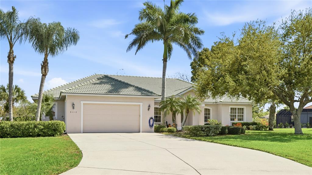 A single-story house with a beige stucco exterior, a tiled roof, and a concrete driveway — 6115 9TH AVENUE CIRCLE NE, BRADENTON, FL