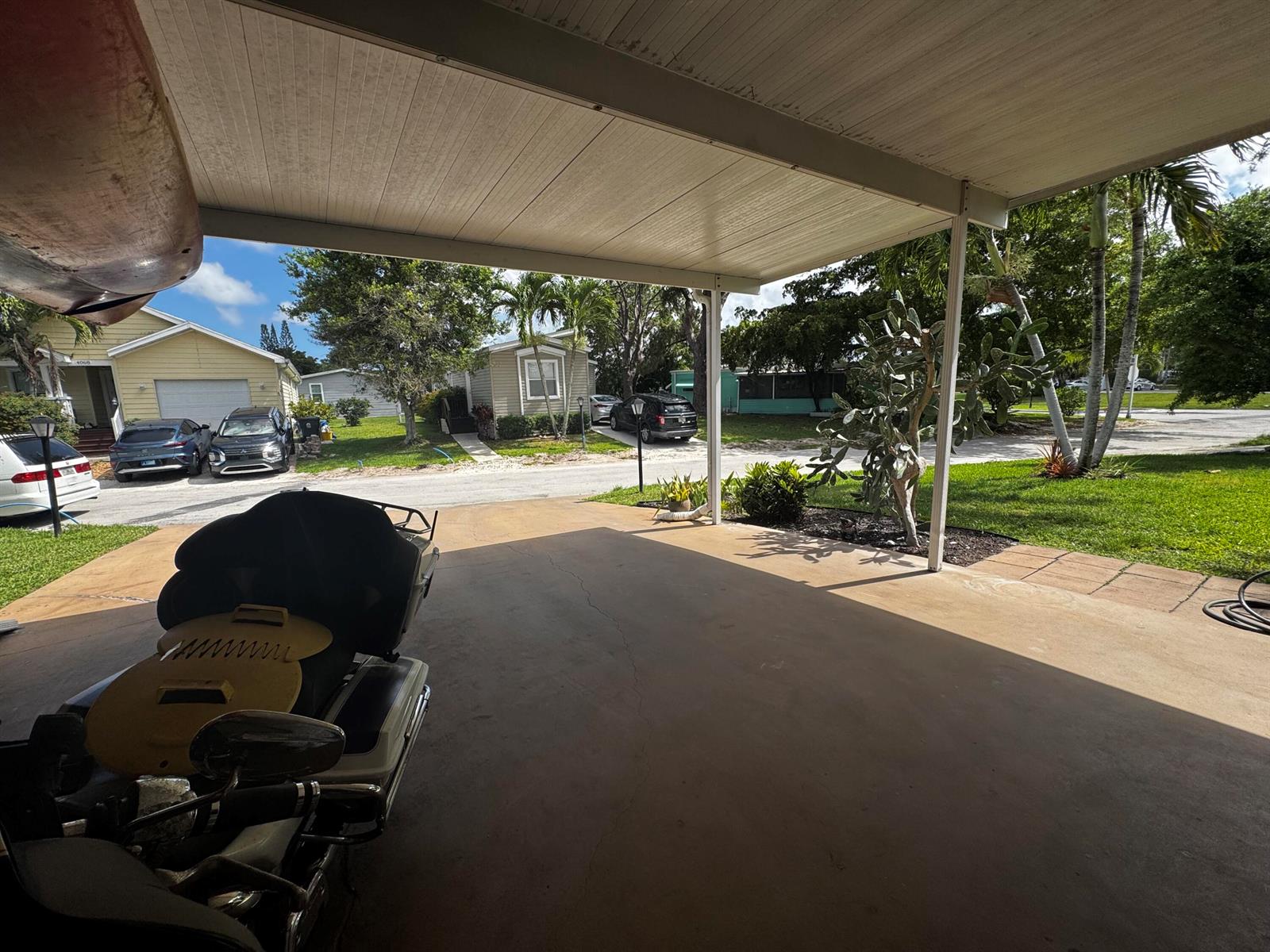 A covered carport area features a concrete floor, a motorcycle, and views of neighboring houses — 4081 4th Court, Lantana FL 33462, LANTANA, FL