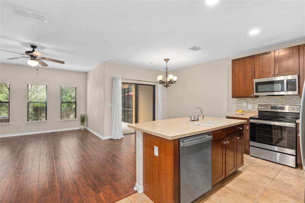 A kitchen with an island and dark wood cabinets opens to a living area with flooring — 6058 TIVOLI GARDENS BOULEVARD, ORLANDO, FL