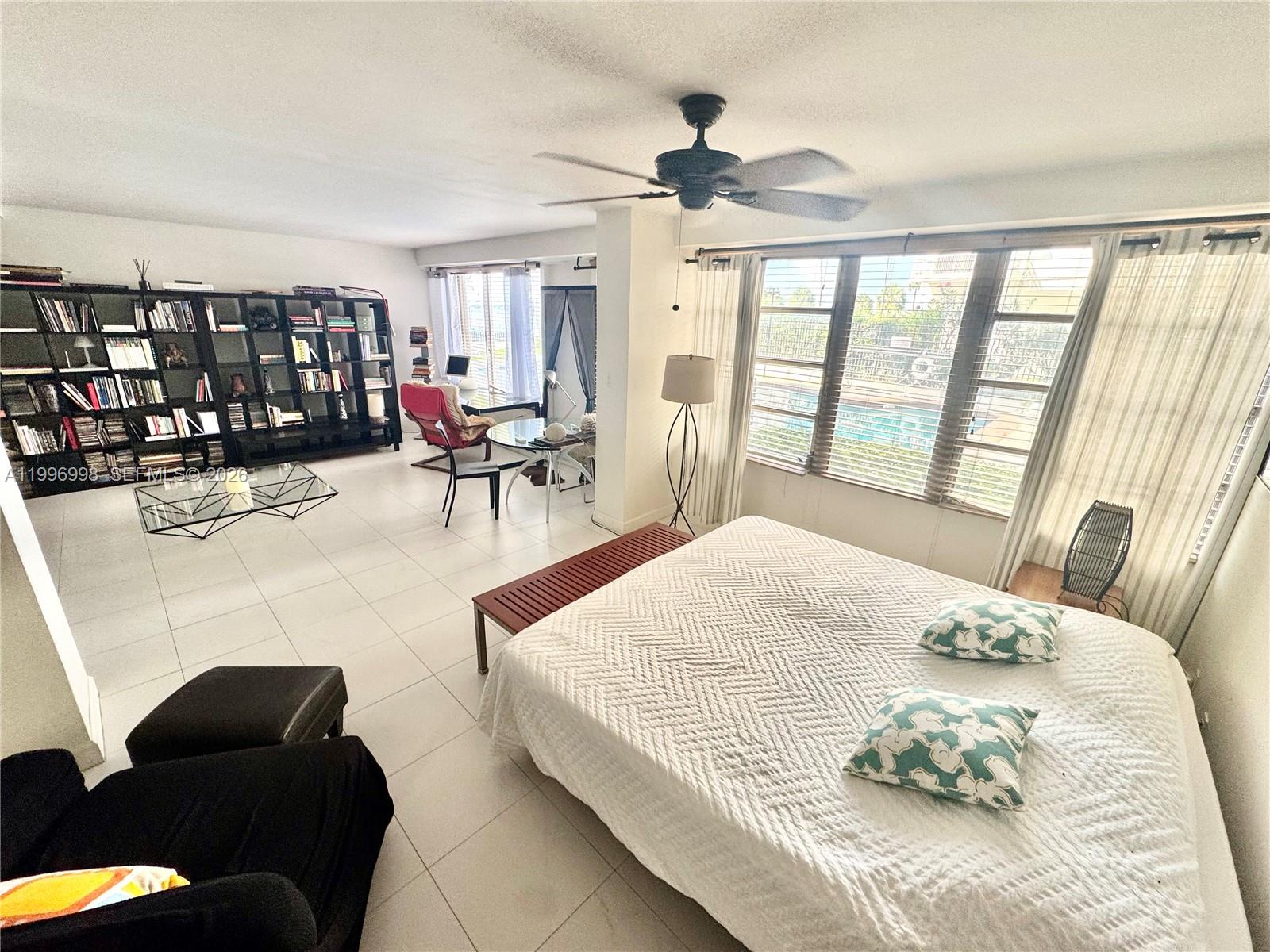 A bedroom features a large bed, tiled flooring, a ceiling fan, and a wall of bookshelves — 1430 Brickell Bay Dr. # 106, Miami FL 33131, MIAMI, FL