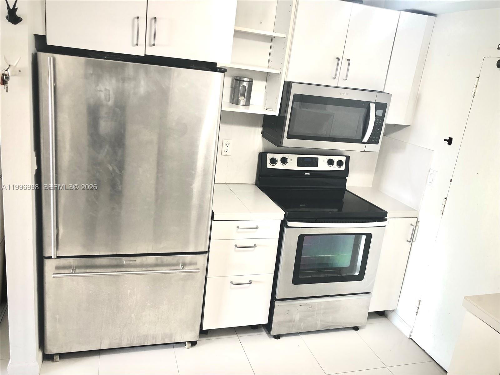 A kitchen features white cabinets, stainless steel appliances, and a tiled floor — 1430 Brickell Bay Dr. # 106, Miami FL 33131, MIAMI, FL