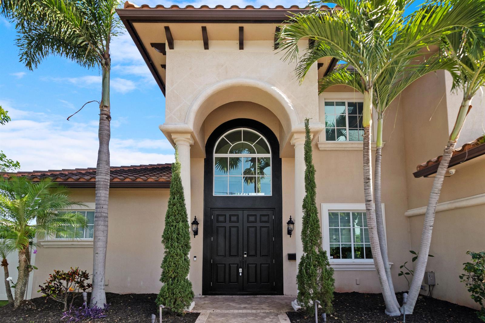 The exterior of a two-story stucco home features a black double door and arched window — 2461 SE 10th Street, Pompano Beach FL 33062, POMPANO BEACH, FL