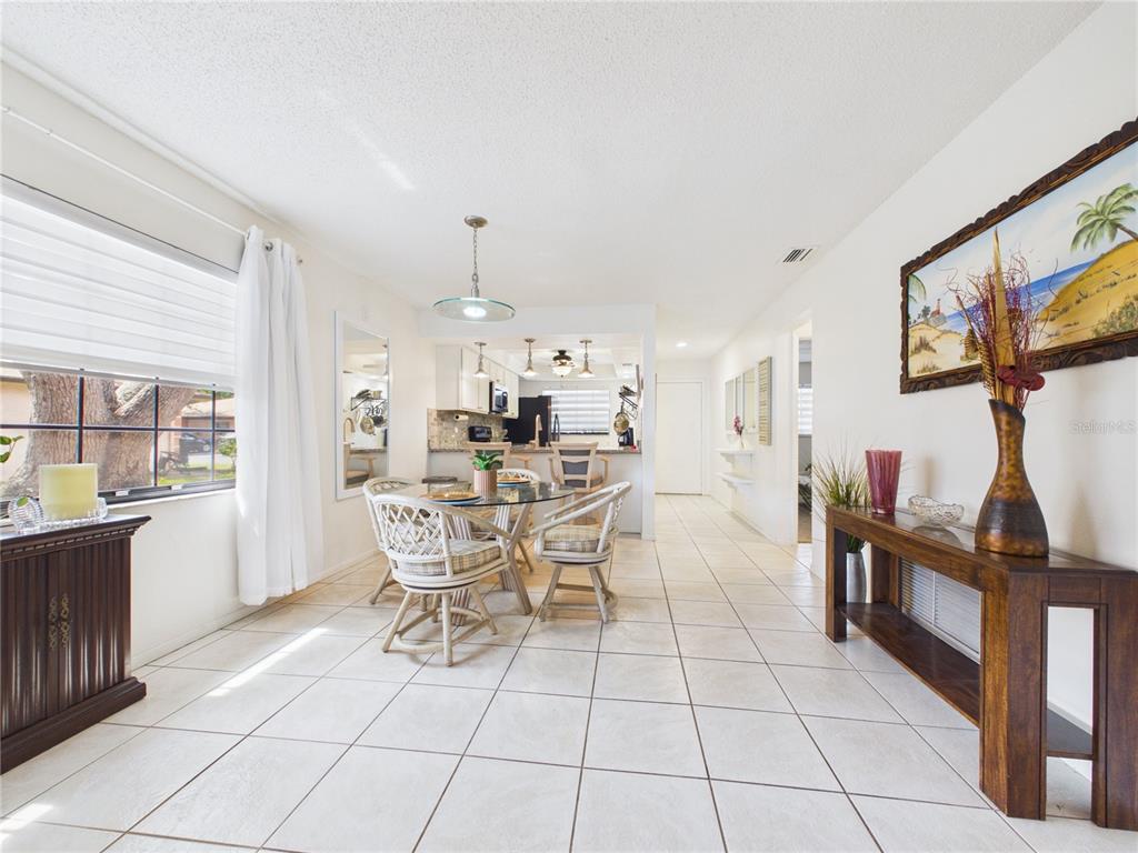 A dining area with a glass table and wicker chairs sits before an open kitchen — 13250 RIDGE ROAD UNIT 9-8, LARGO, FL