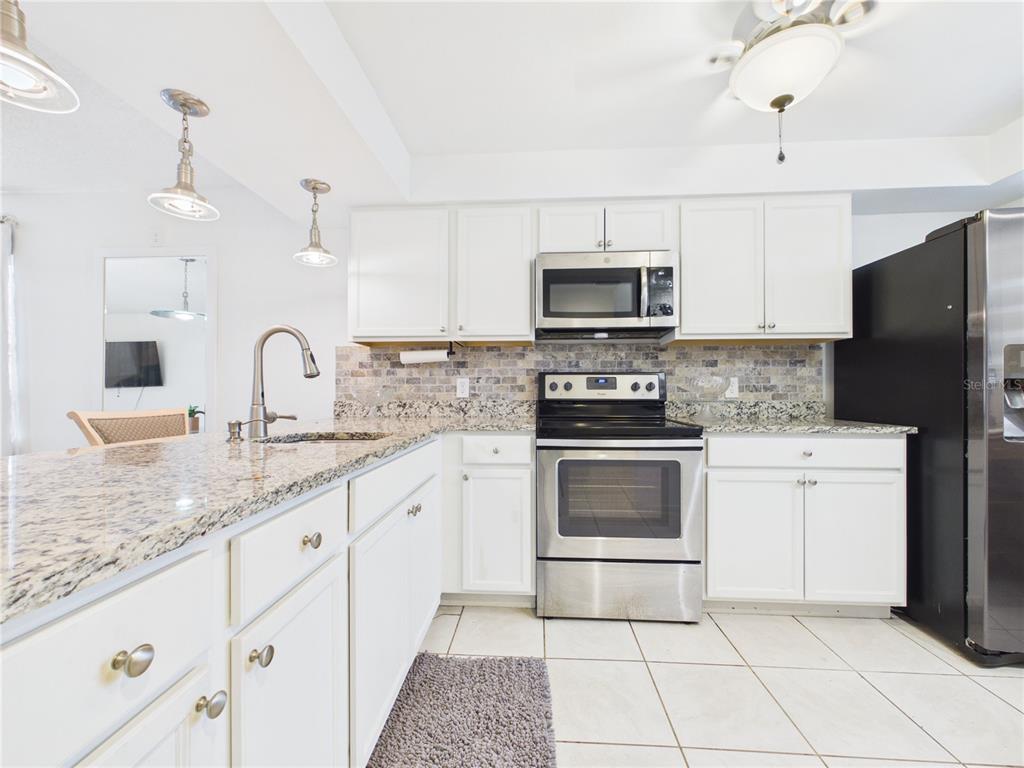 A kitchen features white cabinets, granite countertops, stainless steel appliances, and a tiled floor — 13250 RIDGE ROAD UNIT 9-8, LARGO, FL